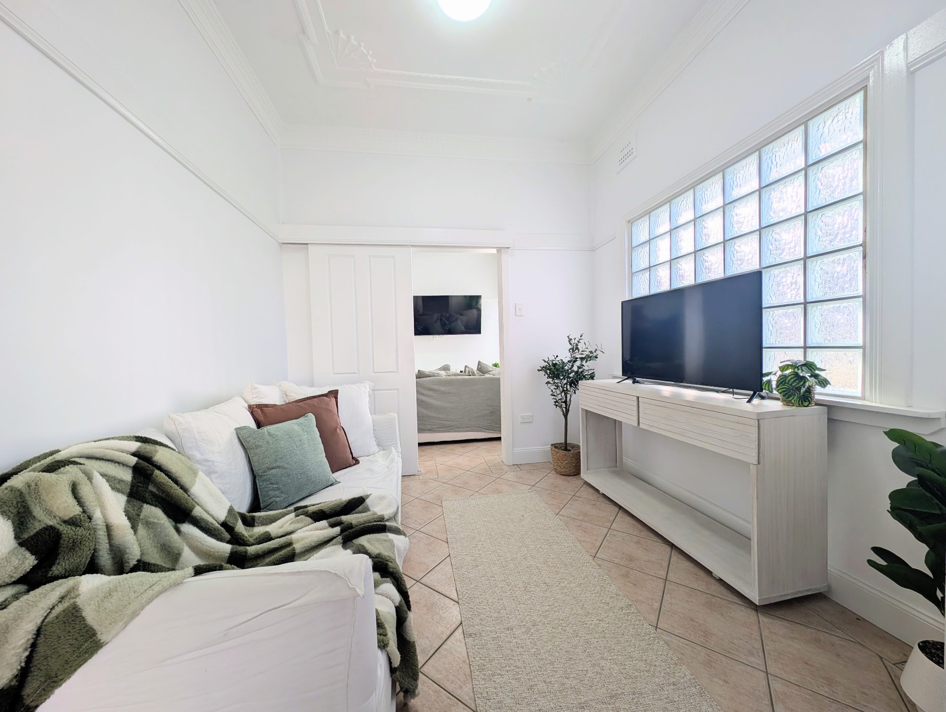 Light-filled lounge with a white sofa and television beside the glass-block window
